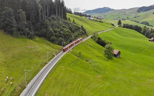 Un train régional dans la campagne. Paysage de collines vertes, avec un village en arrière-plan.